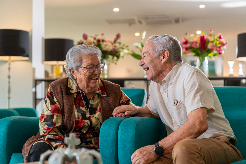 Dos adultos mayores sentados riendo.